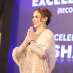 A woman in a traditional outfit with her hands folded in greeting, smiling, on stage at indana palce hotel.